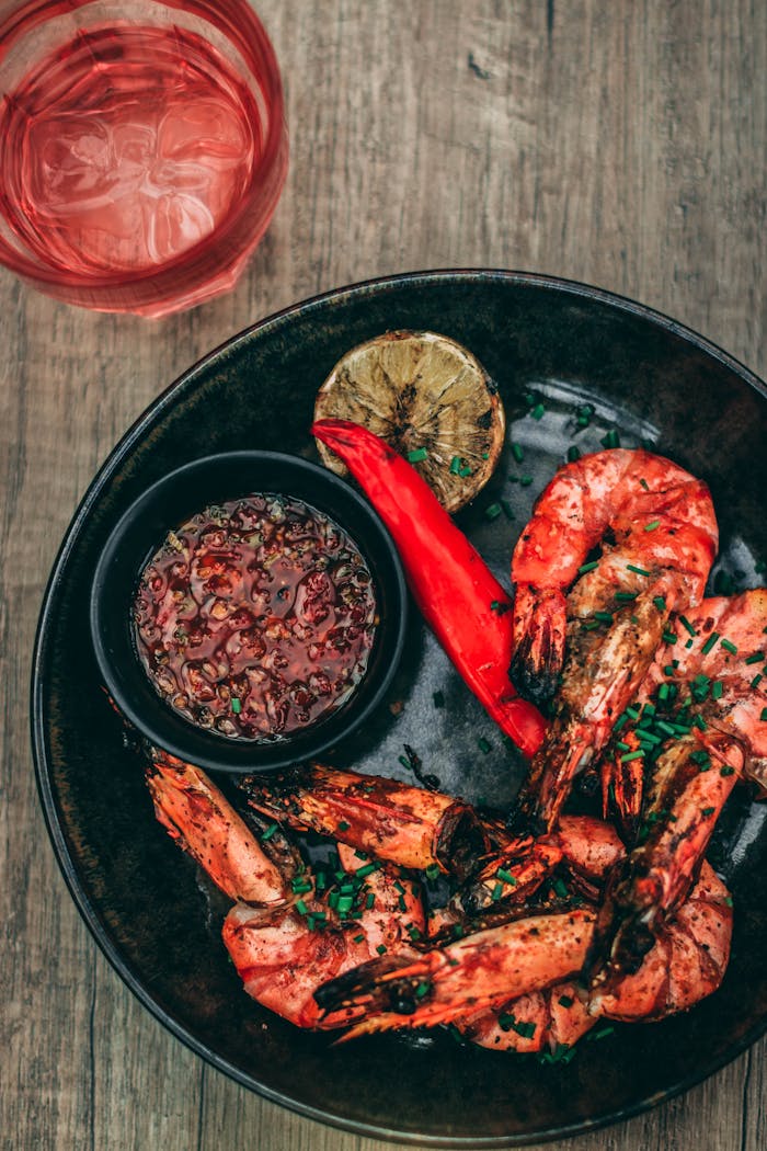 Close-up of spicy grilled shrimp with dipping sauce and grilled lime slice on a plate.